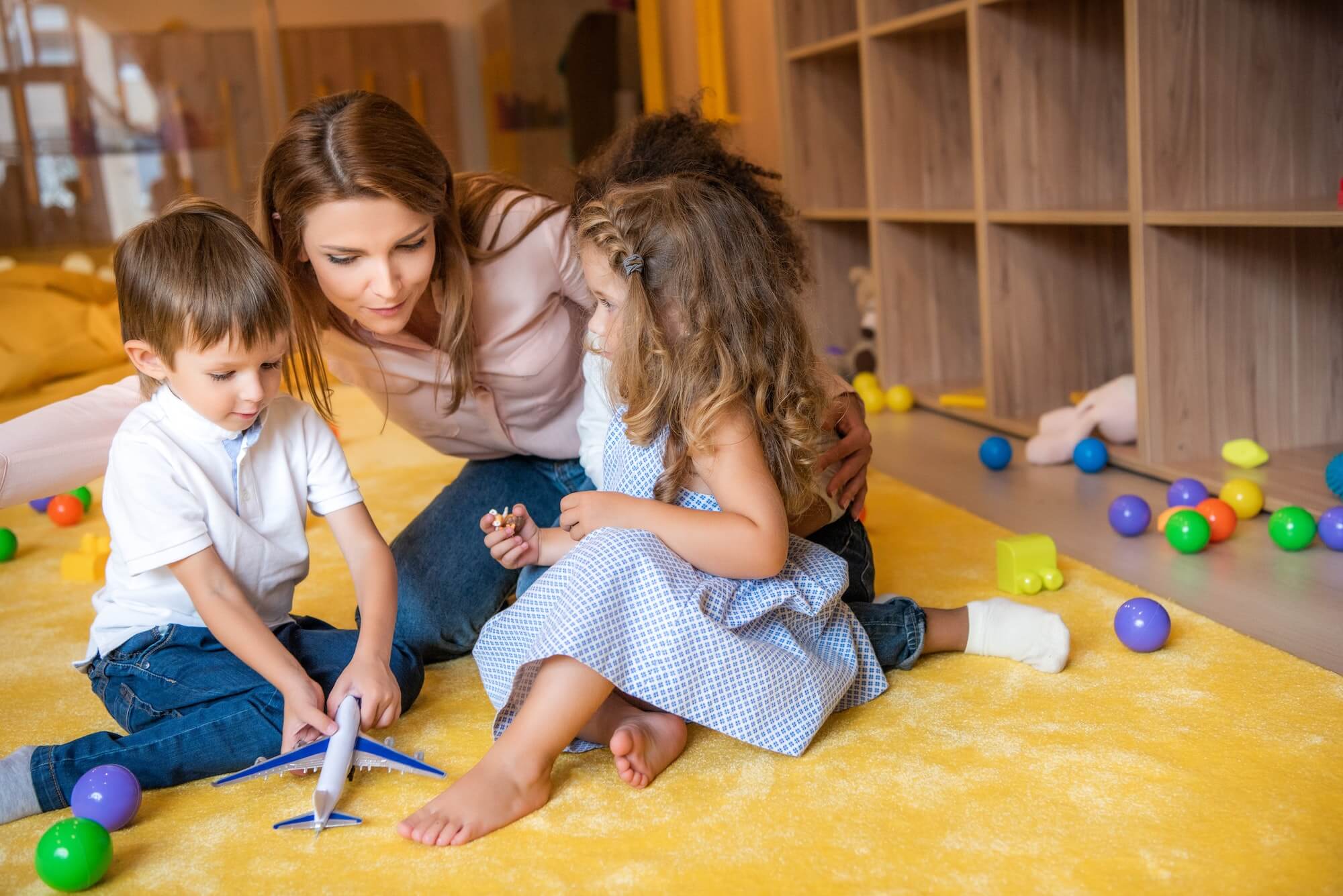 tutor-hugging-adorable-kids-on-carpet-in-kindergarten-1.jpg